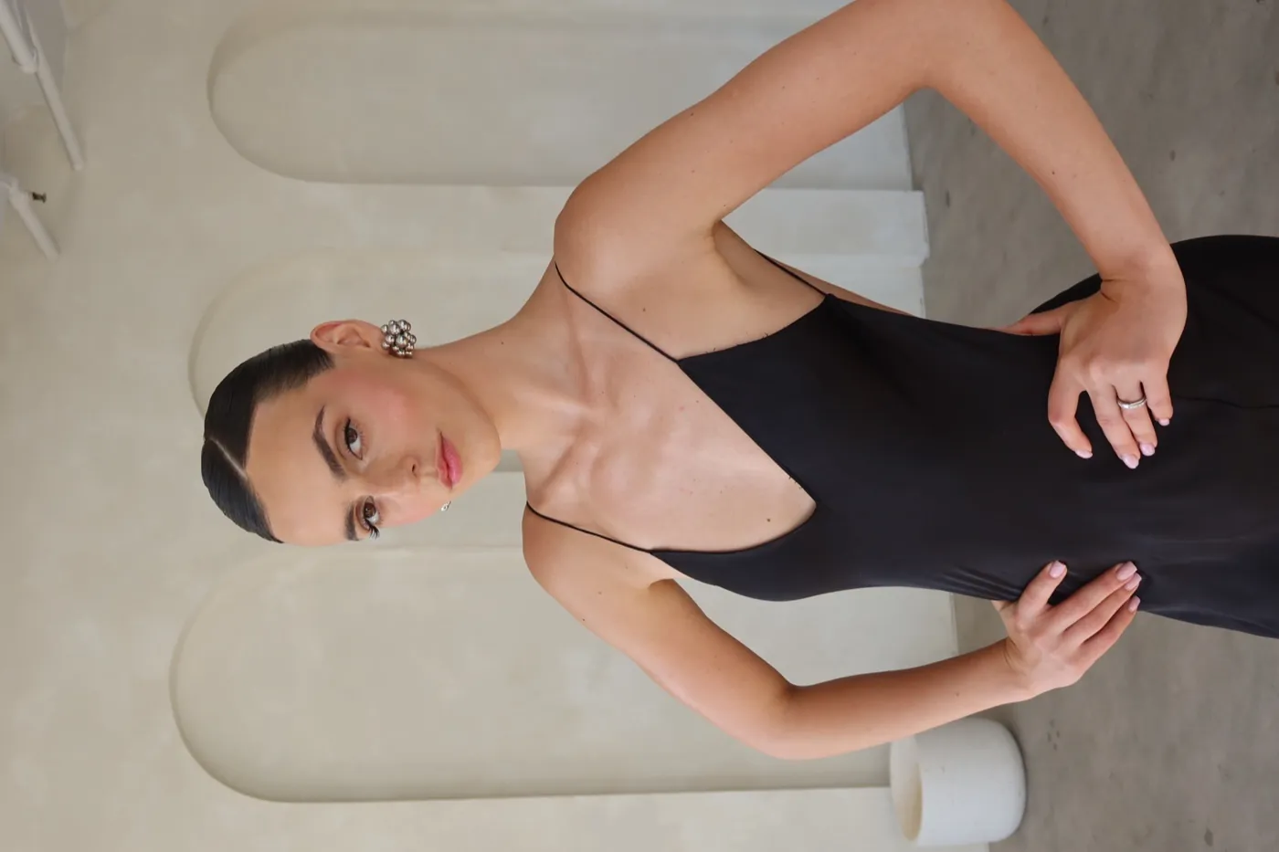 Modelo con slip dress negro y aretes plateados en una habitación con arcos