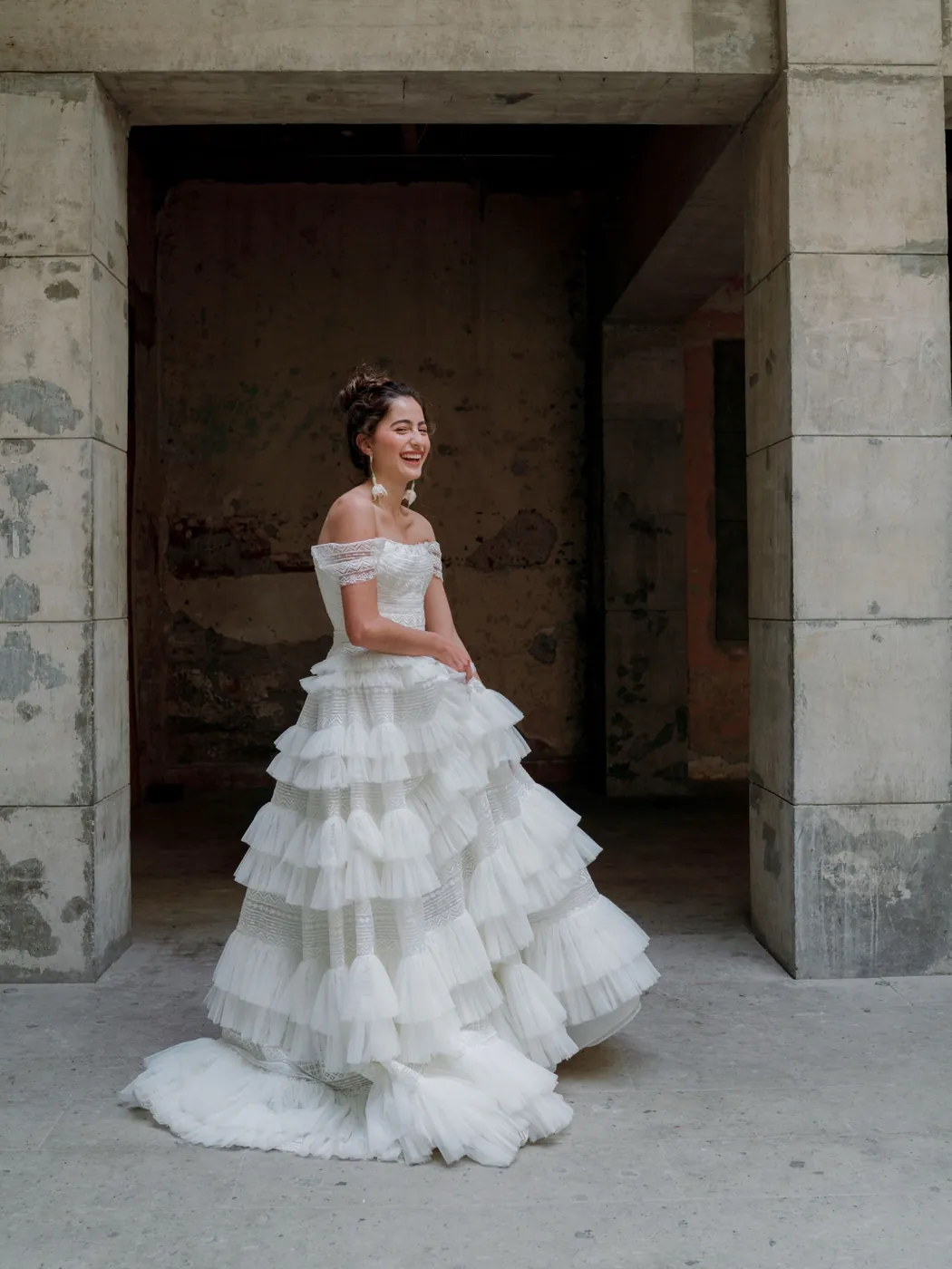 Novia con vestido de capas bajo un arco de piedra