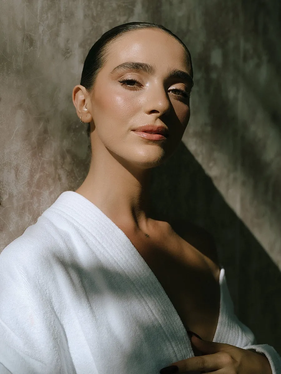 Novia en bata blanca con piel esculpida y luminosa y labios nude suaves