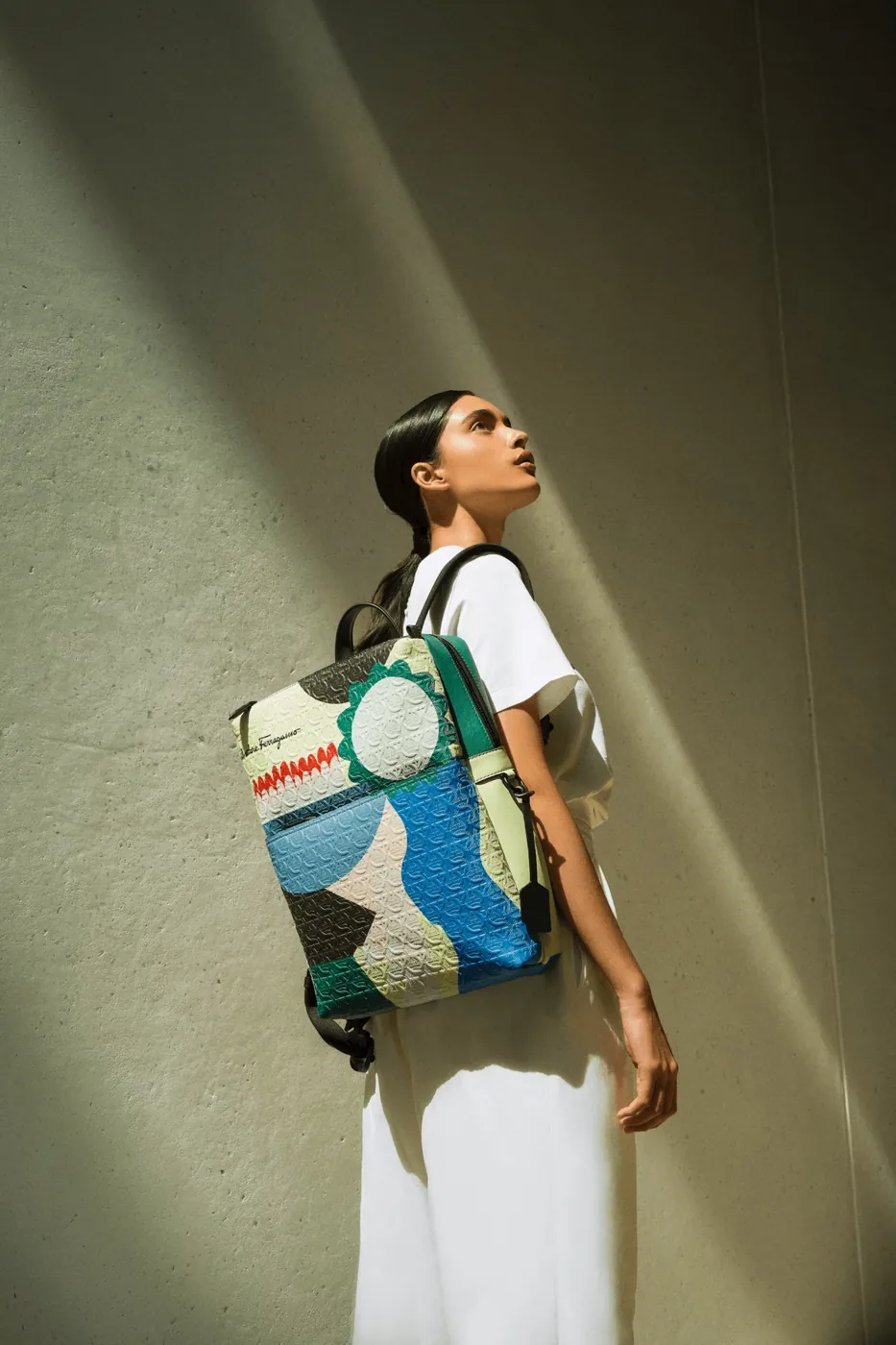 Modelo con coleta baja pulida y mochila de la colección cápsula de Salvatore Ferragamo bajo luz rasante