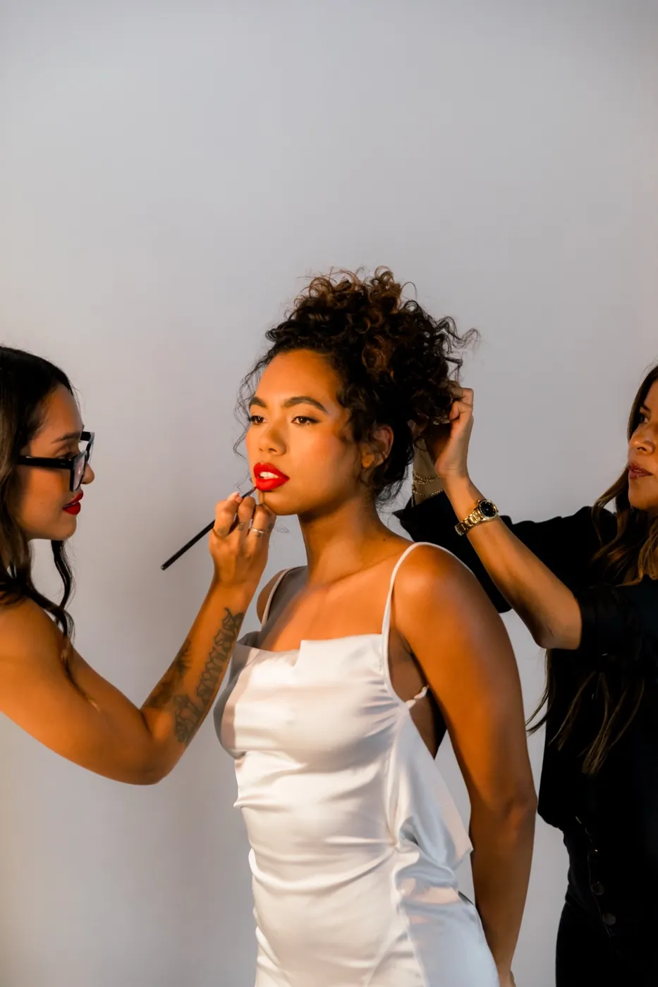 Dos artistas del equipo arreglando a una novia con labios rojos